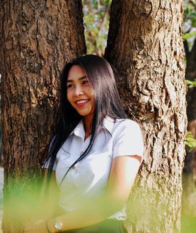 A photo of an Asian woman in a white collared shirt, leaning against a tree