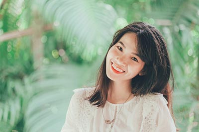 A photo of a smiling Asian woman in a white dress